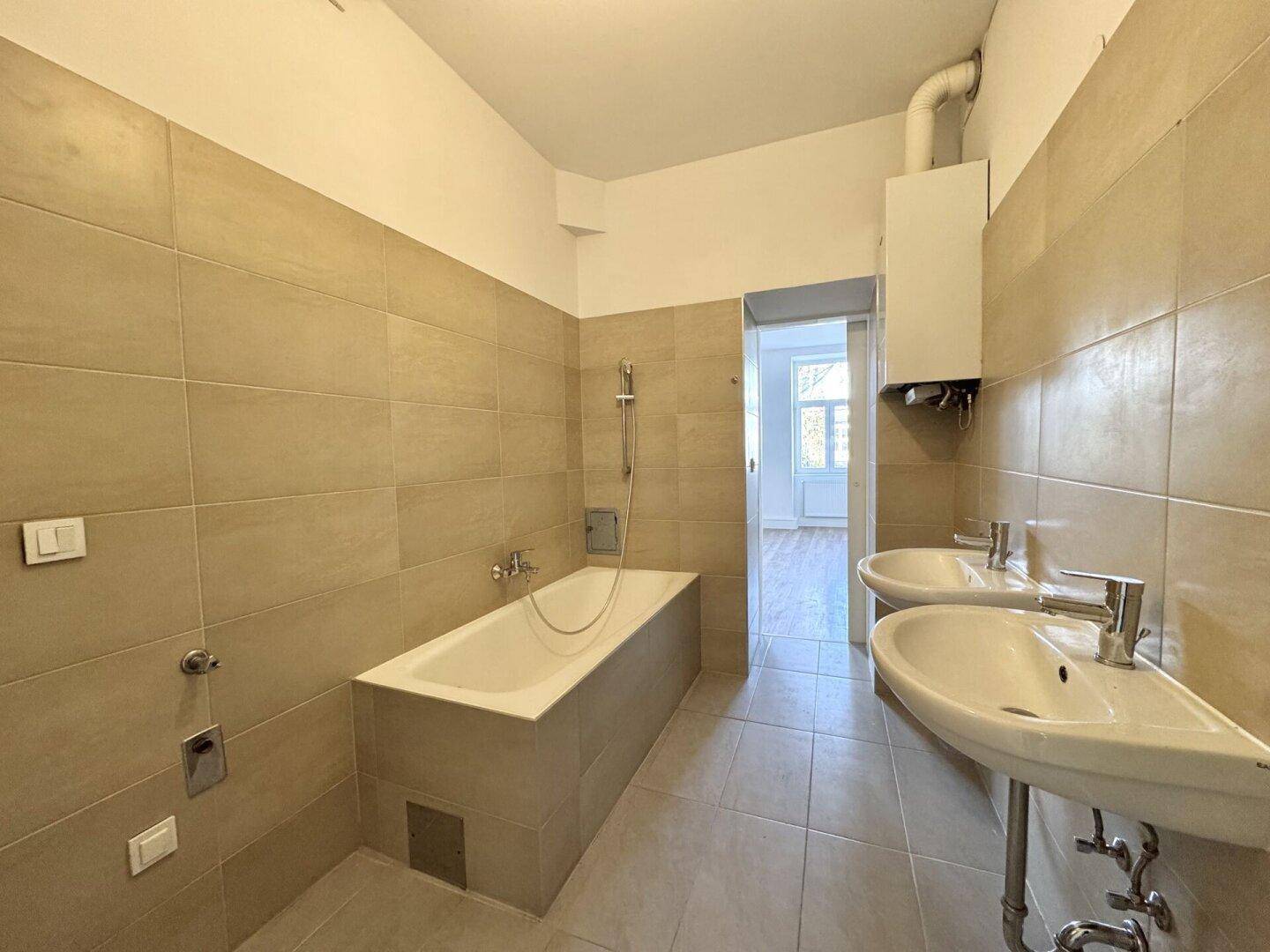 Geräumiges Badezimmer mit zwei Waschbecken, Badewanne und beigefarbenen Fliesen an den Wänden.