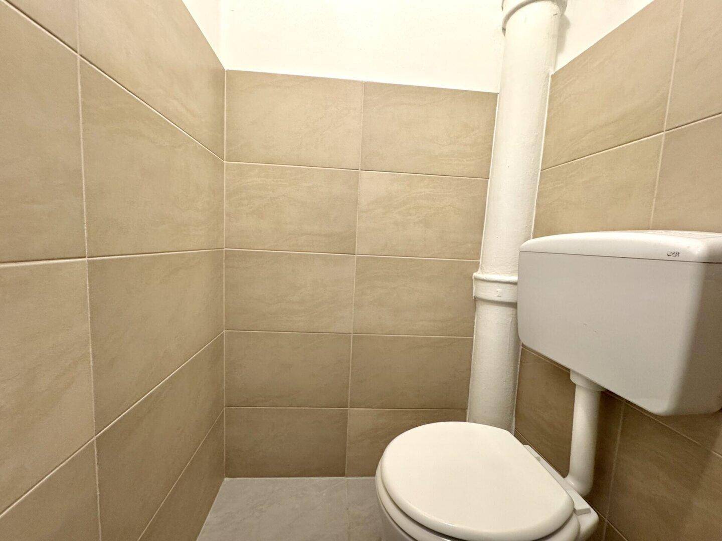 Separates WC mit beigefarbenen Wandfliesen und einer einfachen Toilette in einem kleinen Raum.
