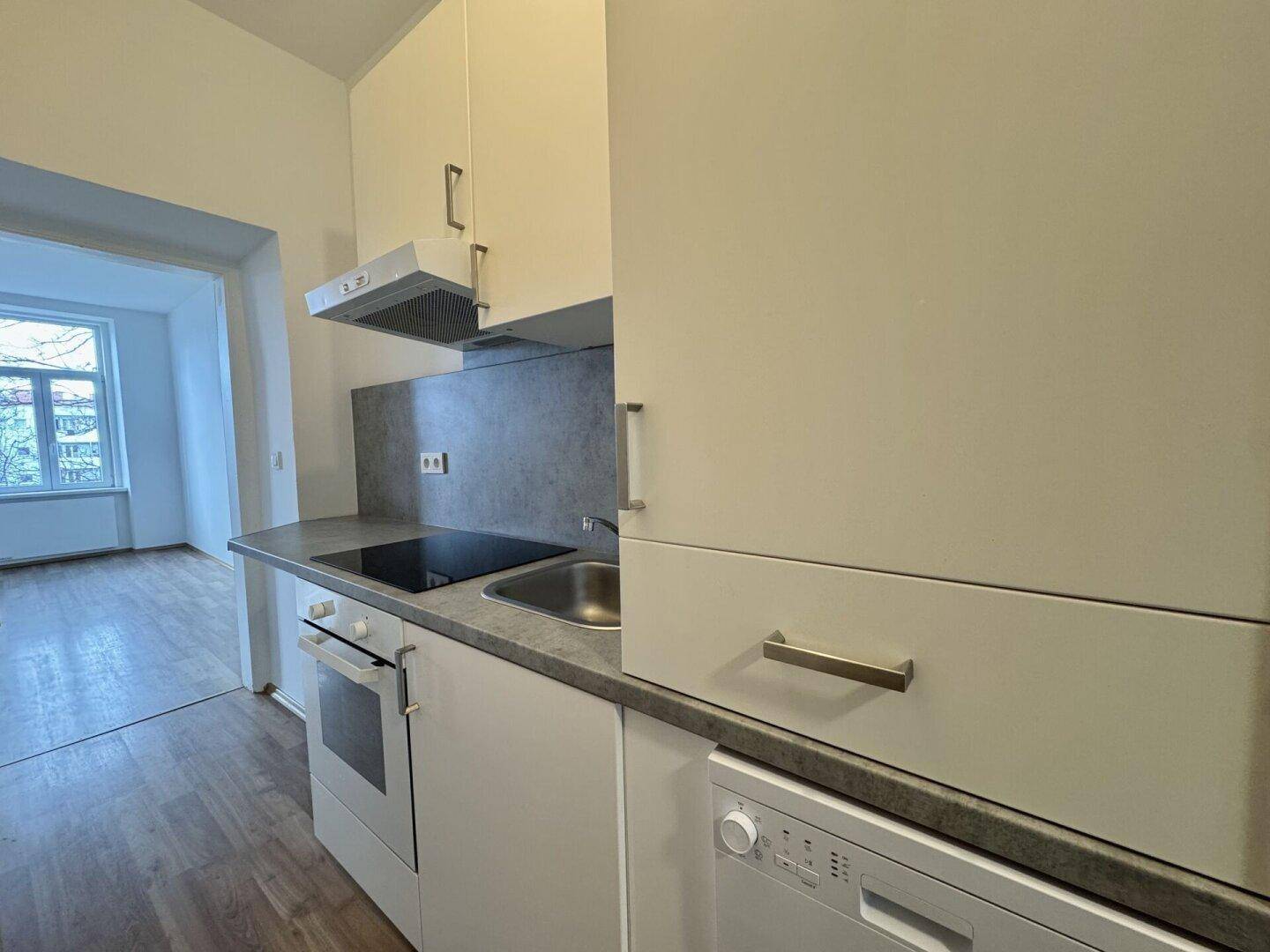 Moderne Einbauküche mit weißen Schränken, Induktionskochfeld und Blick in einen weiteren Raum.