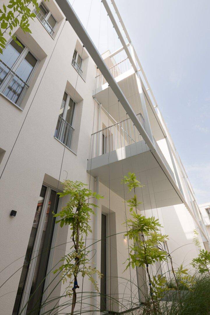 Moderne weiße Gebäudefassade mit Balkonen und großen Fenstern unter blauem Himmel.