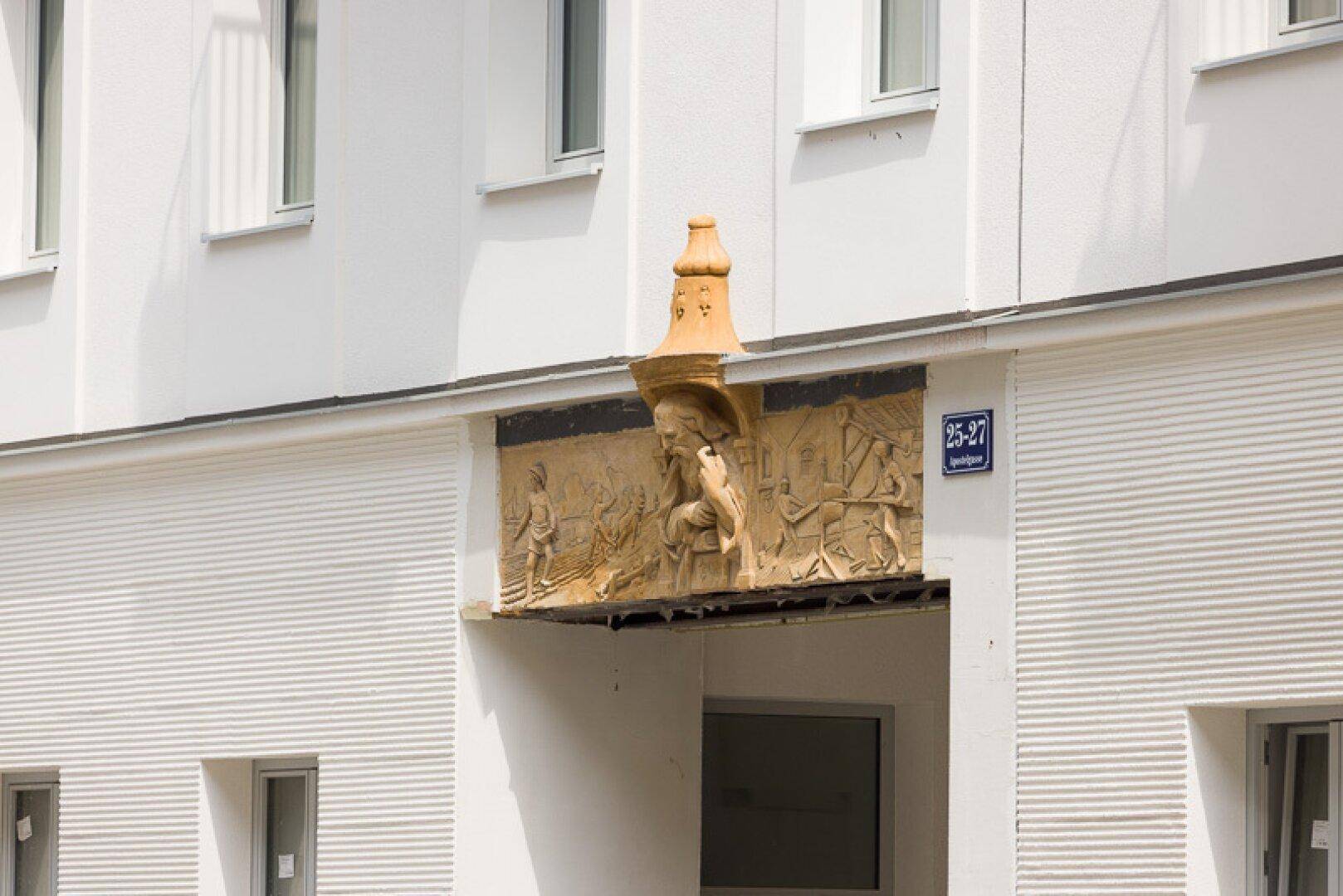 Historisches Relief über einem Durchgang mit figürlichen Darstellungen und Hausnummer.