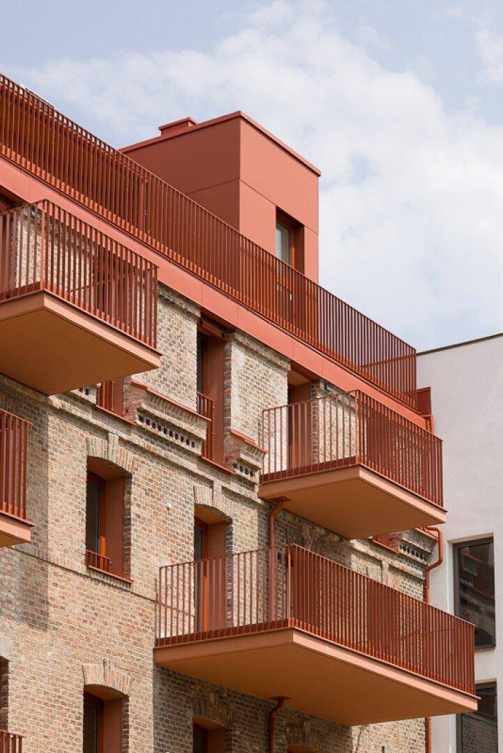 Historische Ziegelfassade mit modernen Balkonen und roten Akzenten, unter blauem Himmel.