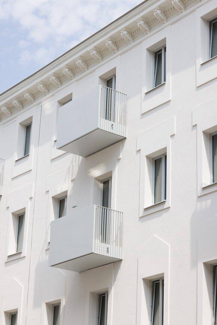 Zwei moderne Balkone mit weißem Geländer an einer hellen Fassade mit dekorativen Elementen.