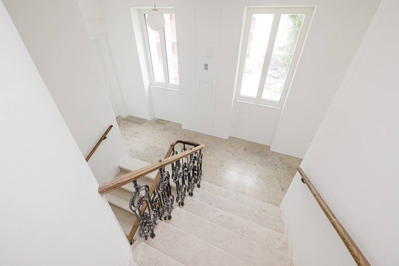 Blick von oben in ein helles Treppenhaus mit Steinstufen und elegantem Geländer.
