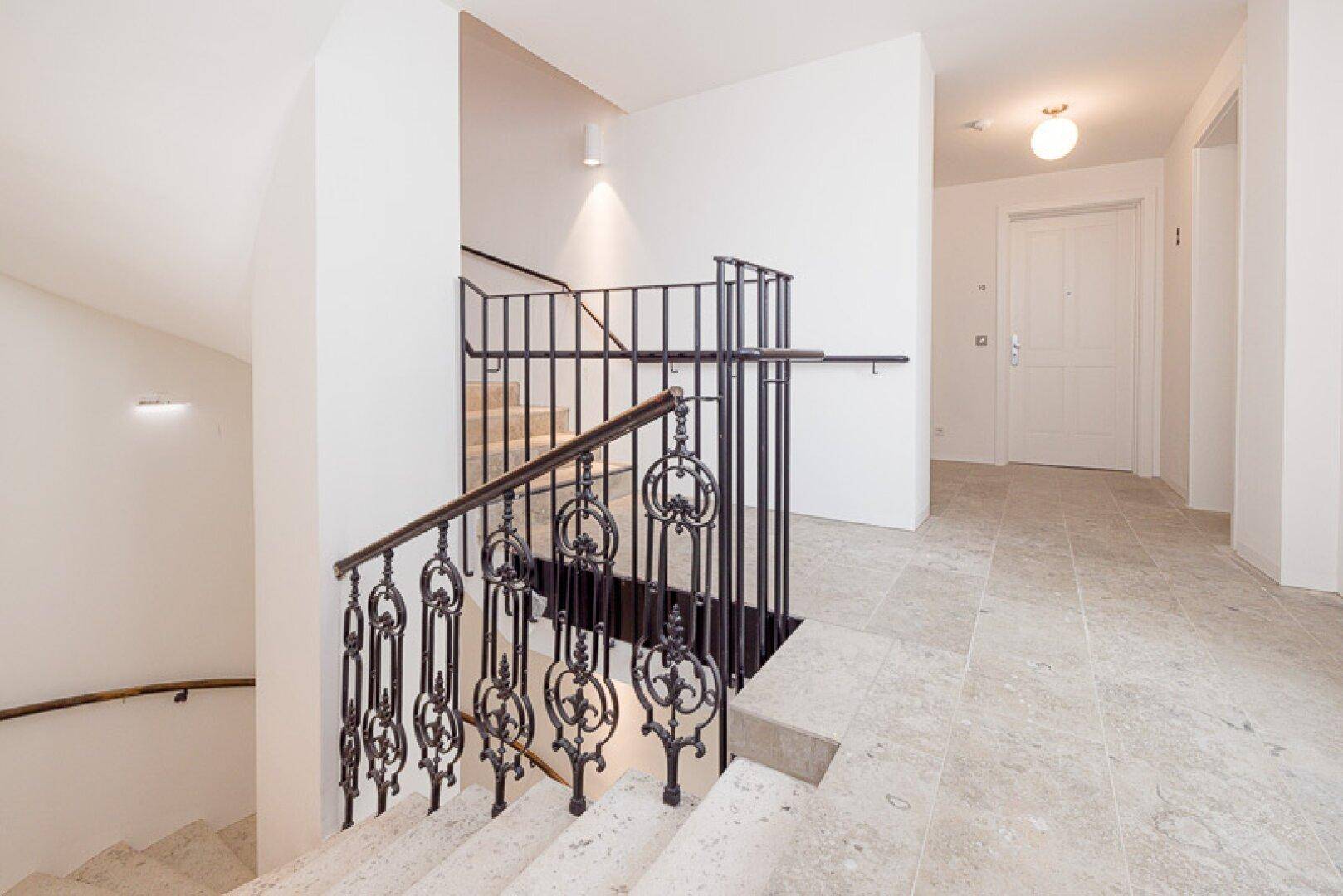 Elegantes Treppenhaus mit Steinstufen, kunstvollem schmiedeeisernem Geländer und hellem Fliesenboden.