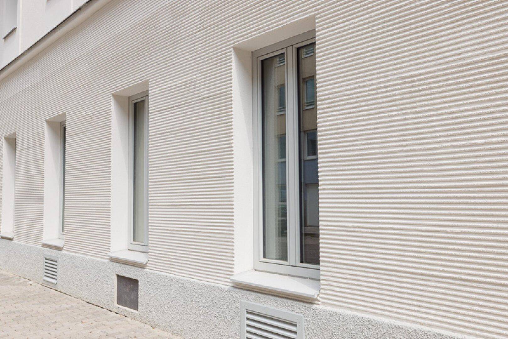 Weiße Fassade mit horizontaler Rillenstruktur und modernen Fenstern.