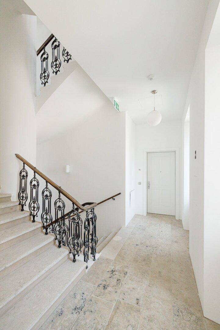 Heller Treppenaufgang mit Steinstufen und einem kunstvoll geschmiedeten Geländer in einem Altbau.