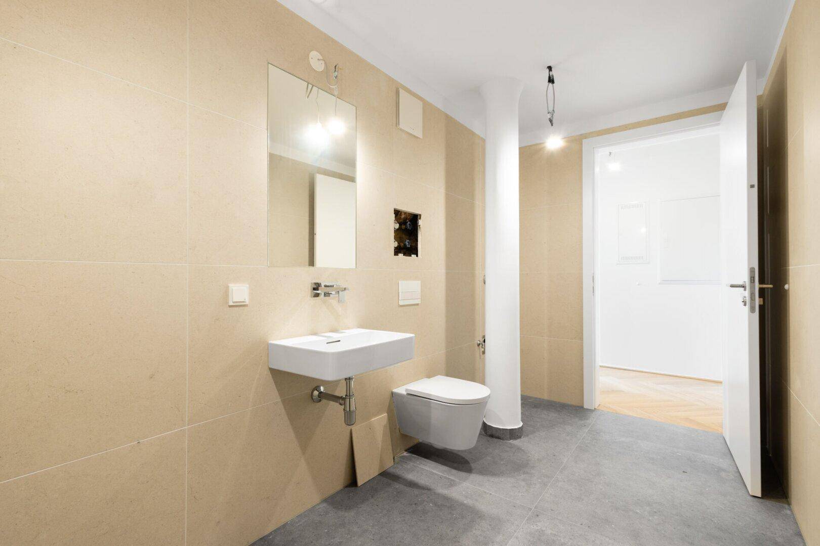 Modernes Badezimmer mit beigefarbenen Fliesen, einem Waschbecken und wandhängendem WC.