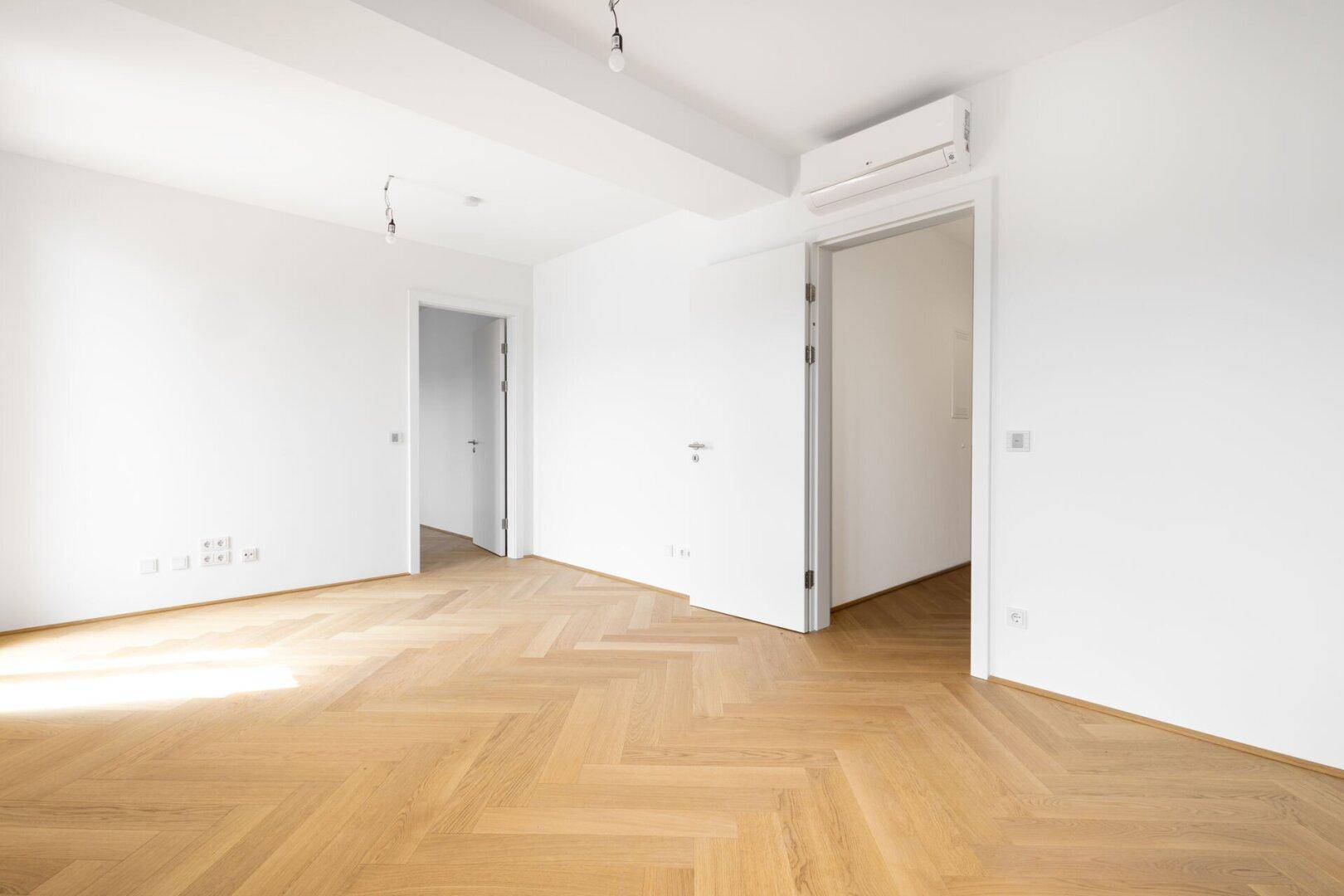 Heller Raum mit Fischgrätparkettboden, weißen Wänden und einer Klimaanlage an der Wand.