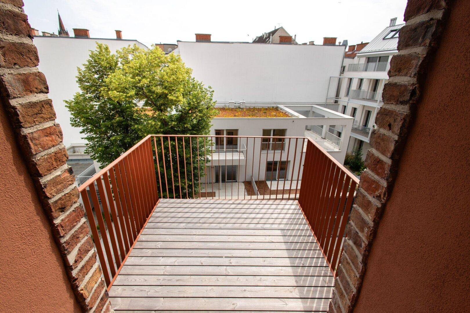 Balkon mit Holzbelag und Metallgeländer, der einen Blick auf den grünen Innenhof bietet.