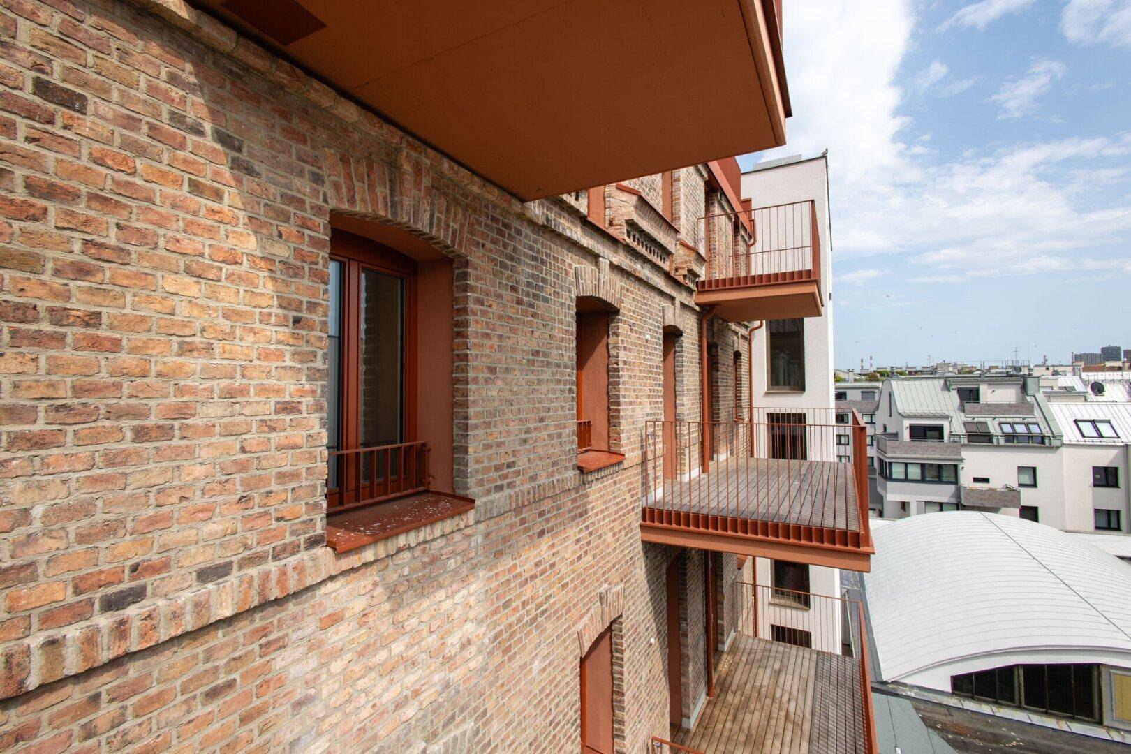 Seitenansicht einer modernen Backsteinfassade mit mehreren Balkonen und Stadtblick.