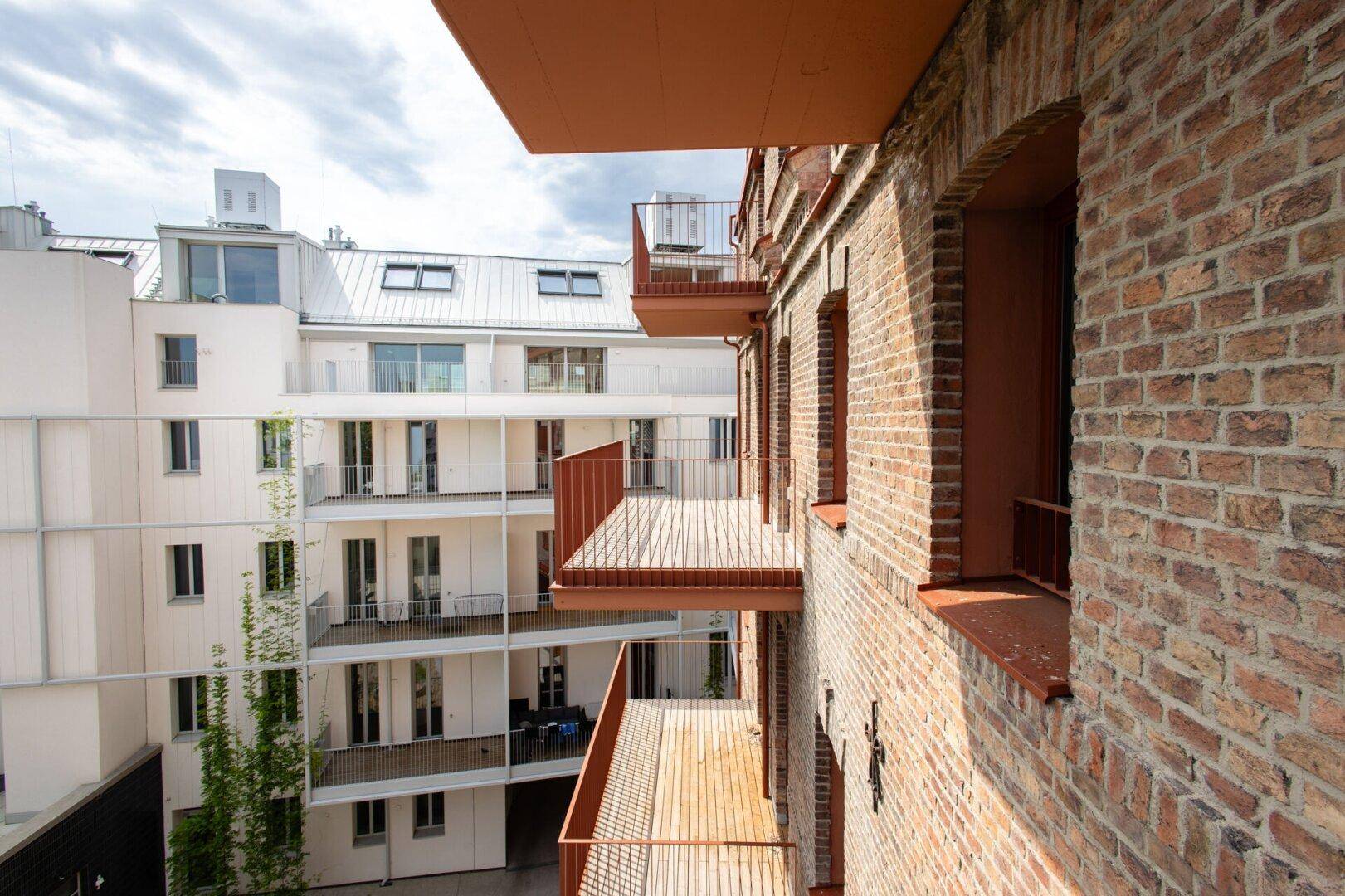 Moderner Gebäudekomplex mit Backsteinfassade, Balkonen und Blick auf einen begrünten Innenhof.