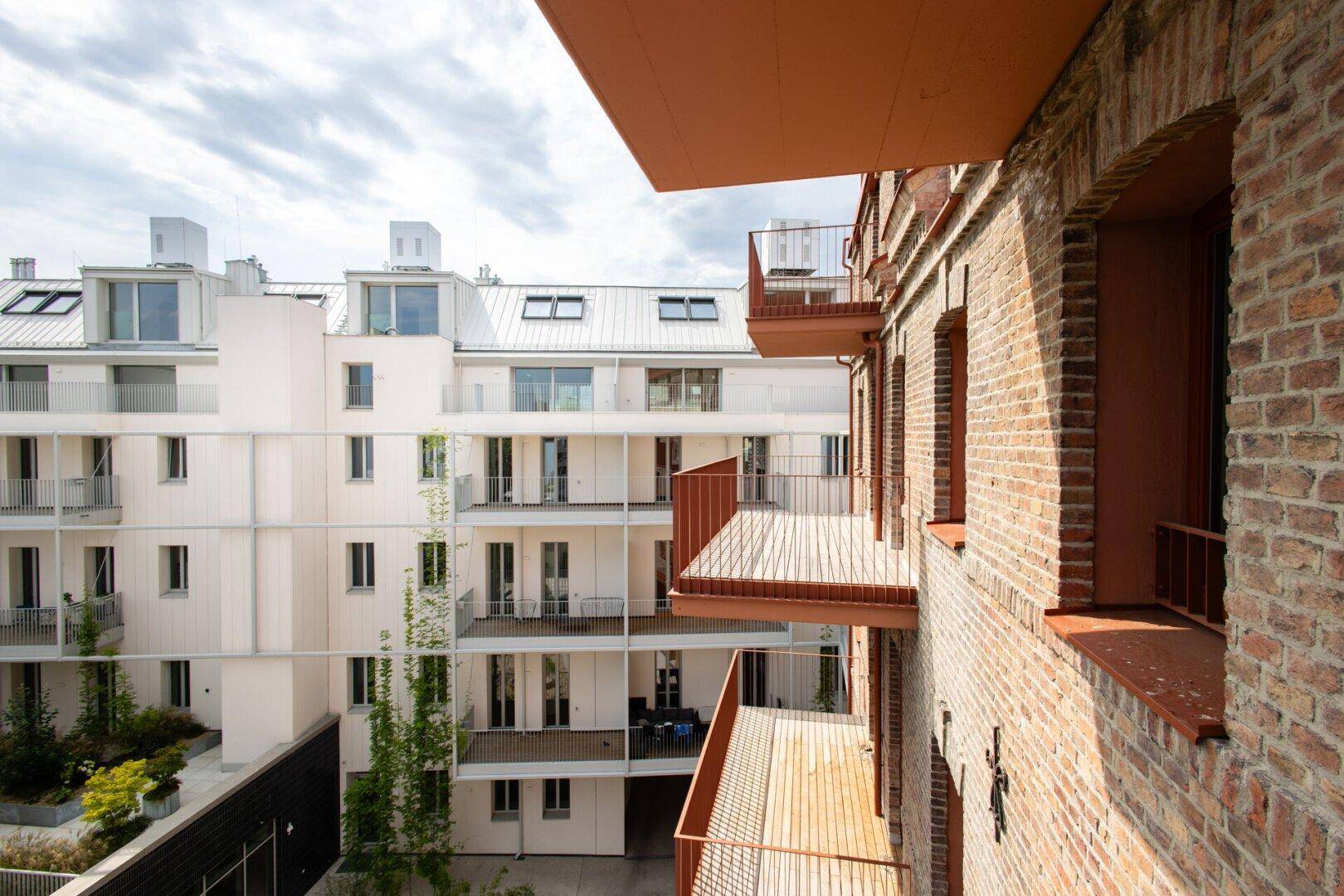 Modernes Wohngebäude mit Backsteinfassade, Balkonen und Blick auf den grünen Innenhof.