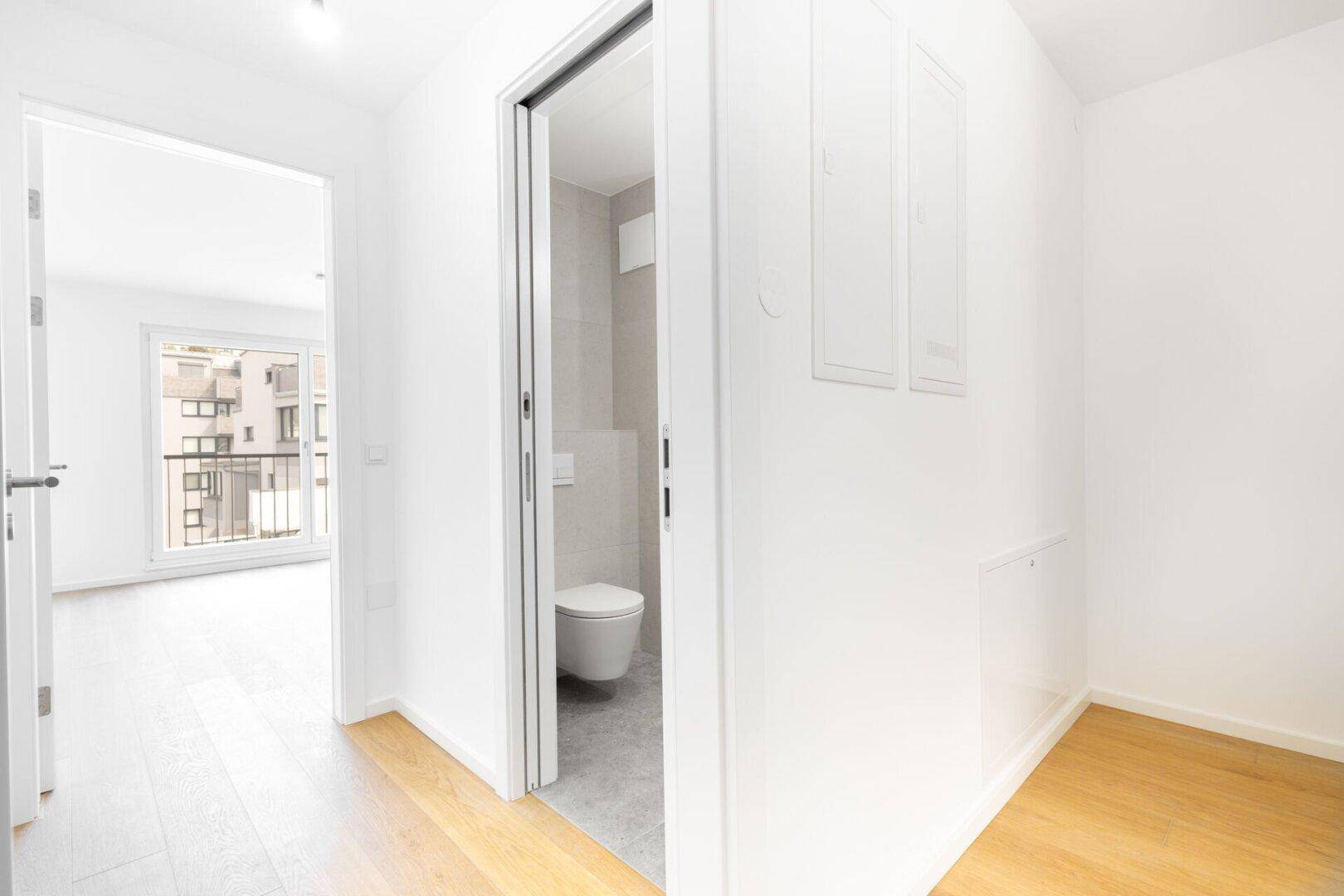 Heller Flur mit Parkettboden und Blick in ein modernes Badezimmer.