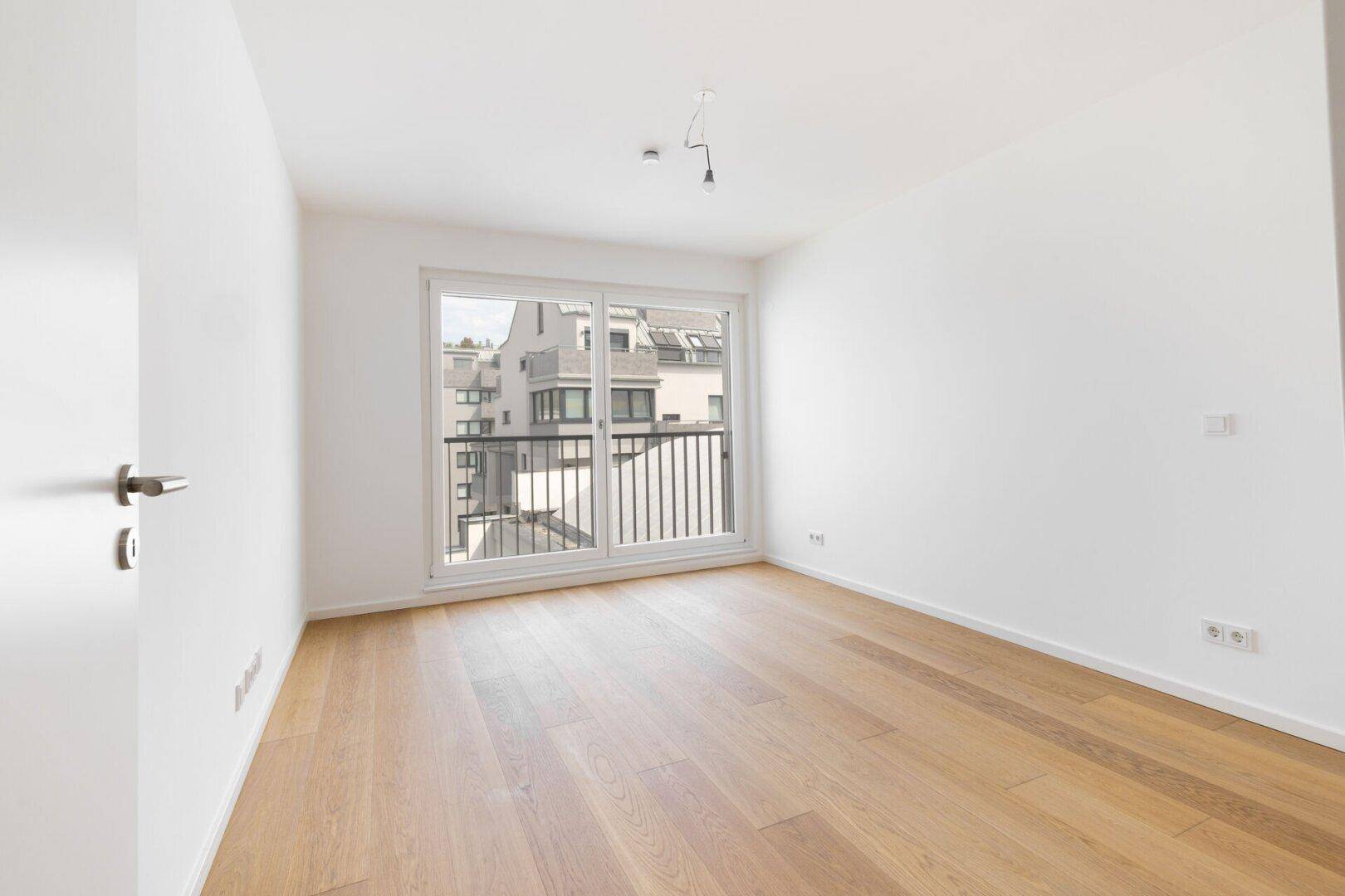 Helles Zimmer mit Parkettboden und Zugang zu einem französischen Balkon.