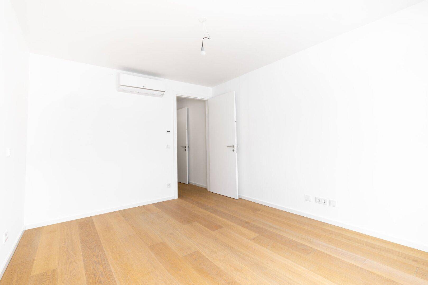 Geräumiges Zimmer mit Parkettboden, Klimaanlage und weiß gestrichenen Wänden.