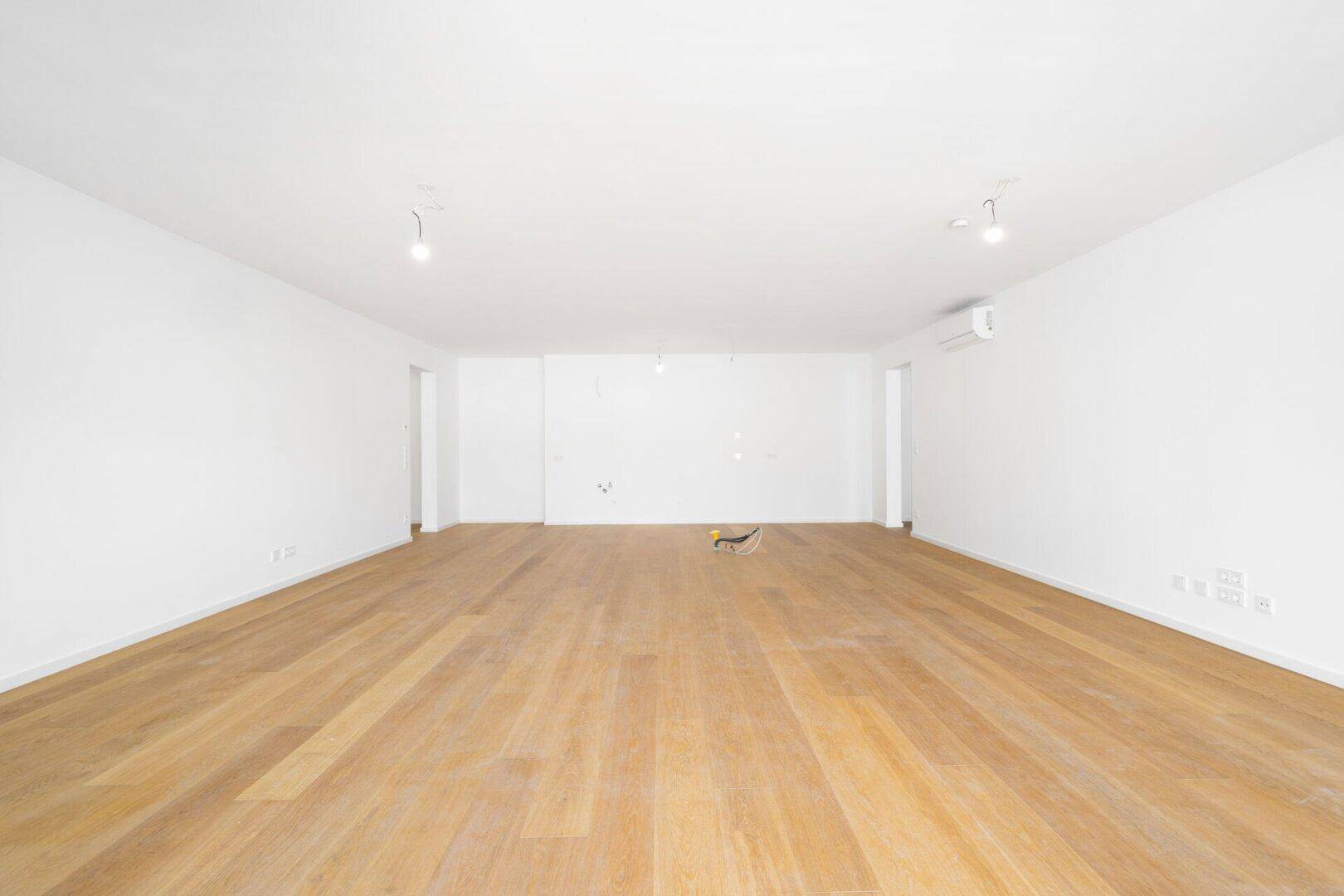 Weitläufiger Wohnbereich mit Parkettboden, Klimaanlage und viel natürlichem Licht.