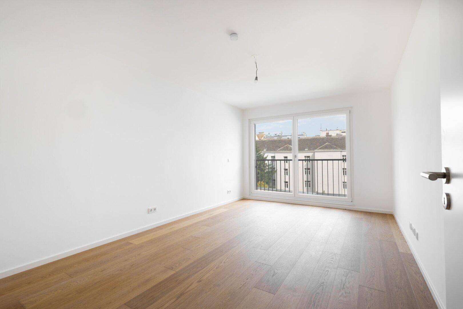 Helles Zimmer mit Parkettboden und großen Fenstern mit Stadtblick.