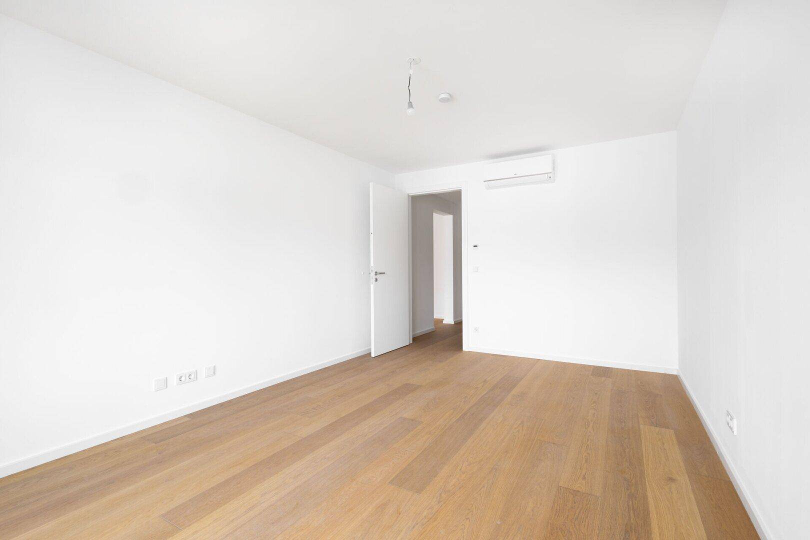 Helles Zimmer mit Parkettboden, Klimaanlage und weiß gestrichenen Wänden.