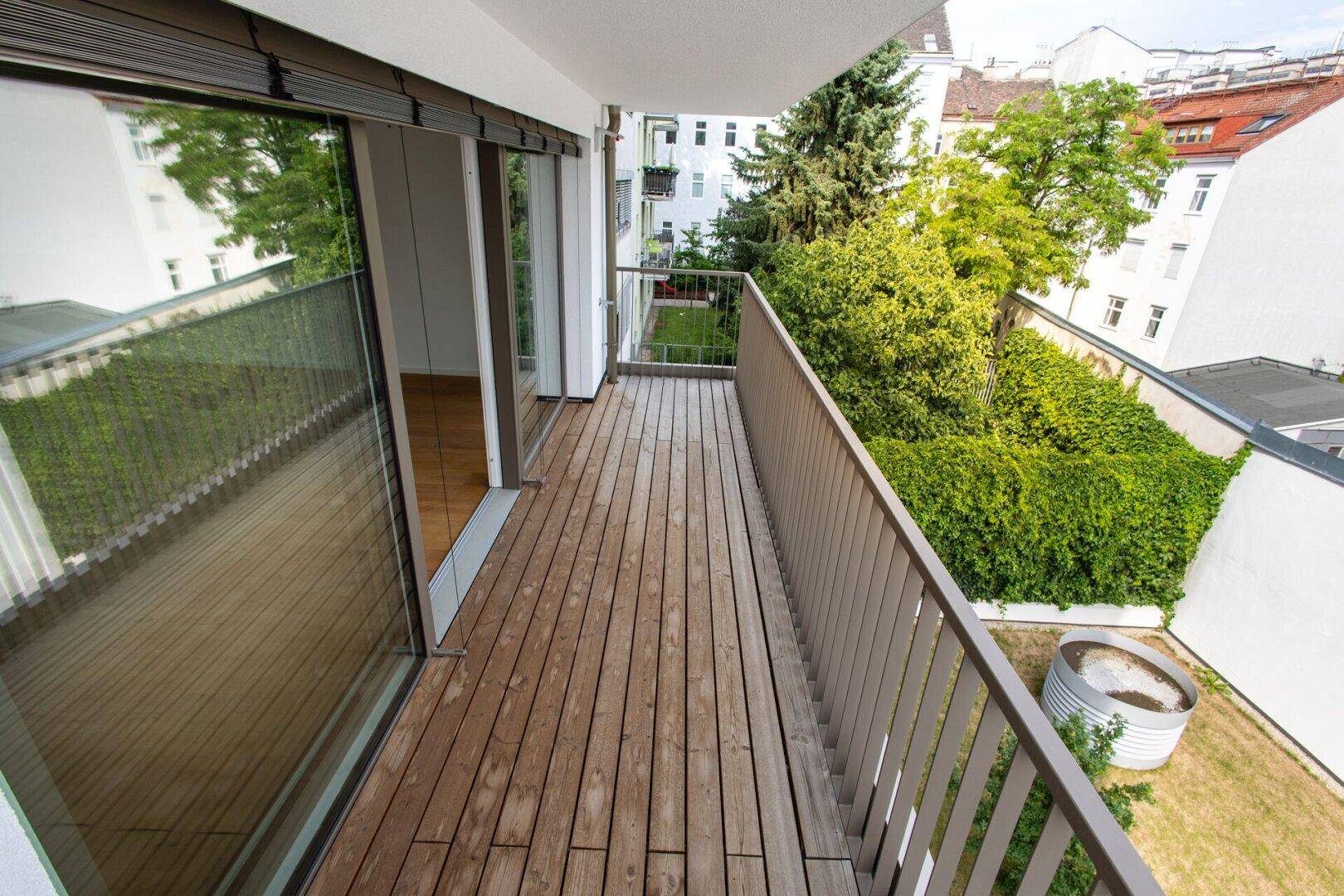 Balkon mit Holzboden und Blick auf den begrünten Innenhof und Gartenbereich.