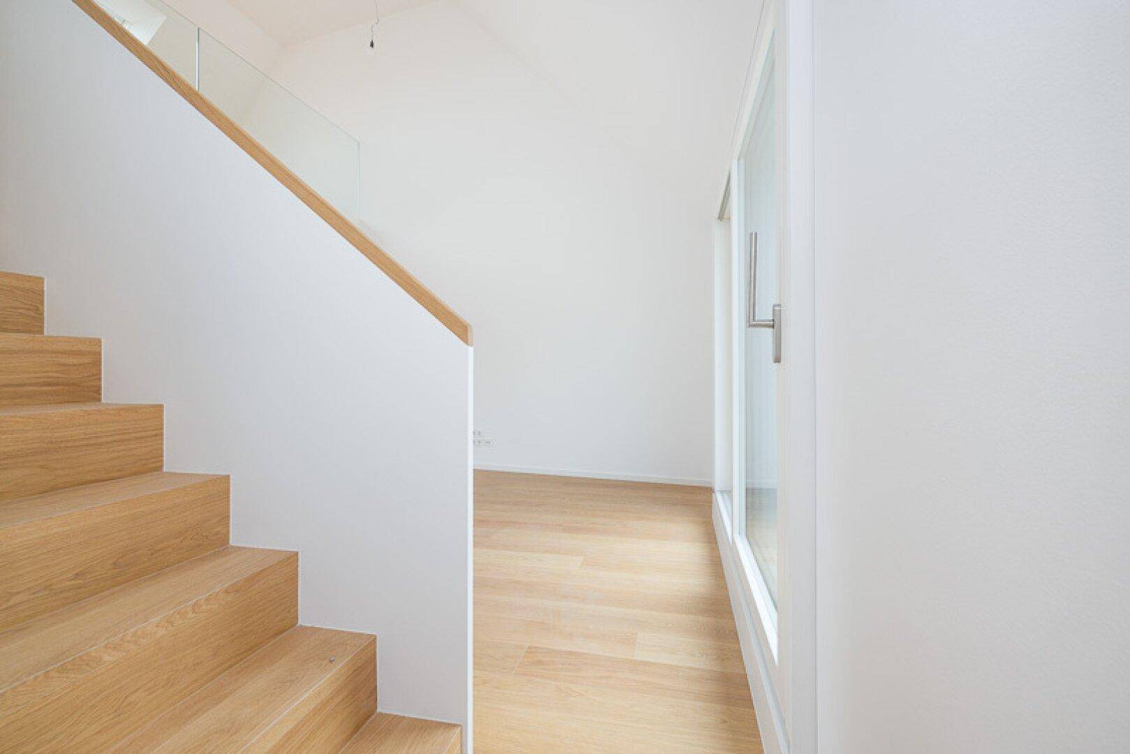 Moderner Treppenbereich mit Holzstufen und weißer Wand, daneben ein großes Fenster.