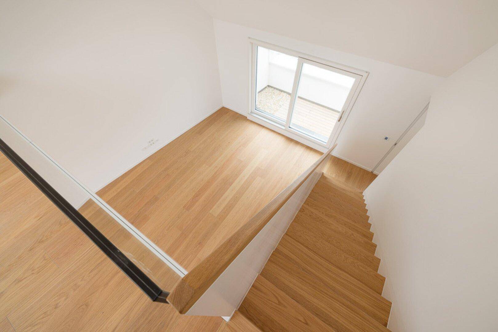 Heller Treppenaufgang mit Holzstufen und Glasgeländer, der zu einem weiteren Raum führt.