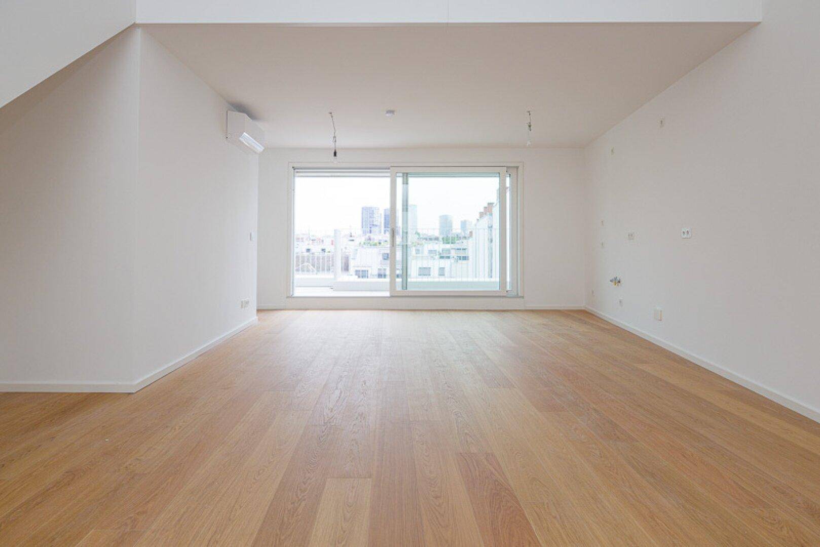 Heller Wohnbereich mit Holzparkett und großen Schiebetüren, die einen Stadtblick bieten.