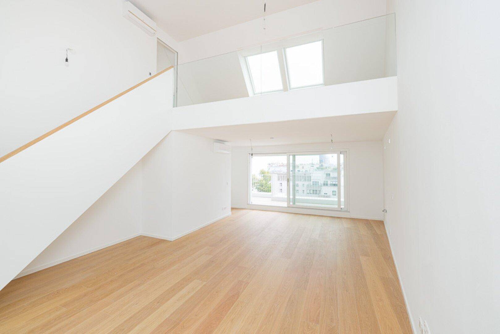 Offener Wohnbereich mit Holzparkett, hohen Decken und einer Galerie mit Dachfenstern.