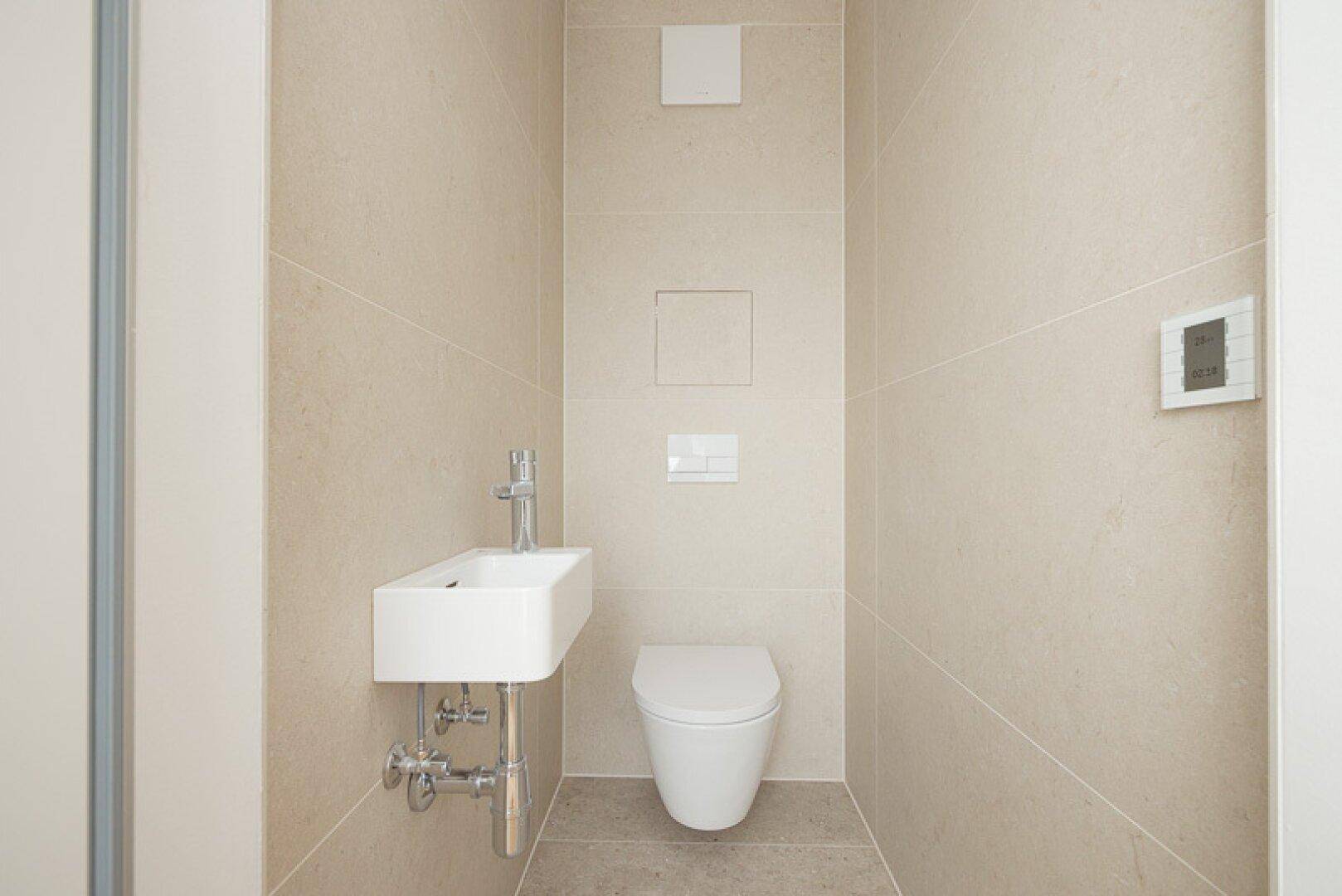 Modernes Gäste-WC mit beigefarbenen Fliesen, wandhängendem WC und kleinem Waschbecken.