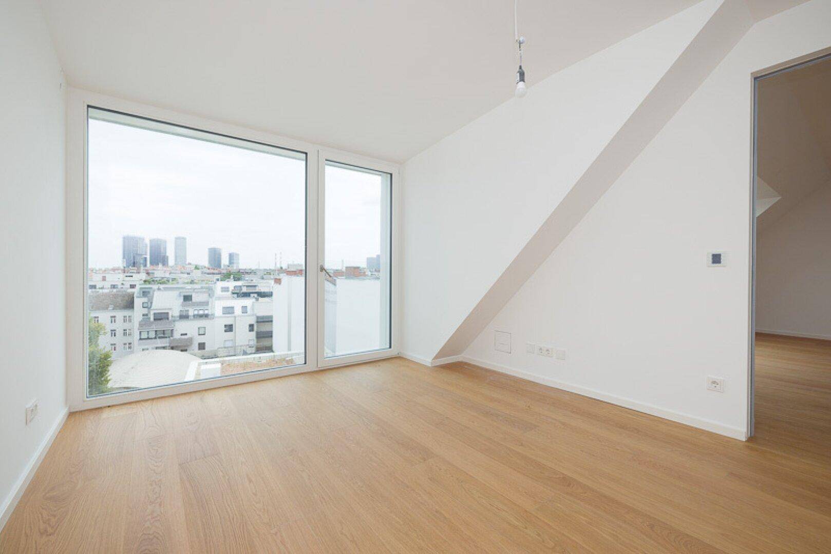 Helles Schlafzimmer im Dachgeschoss mit Holzparkett und großem Fenster mit Stadtblick.
