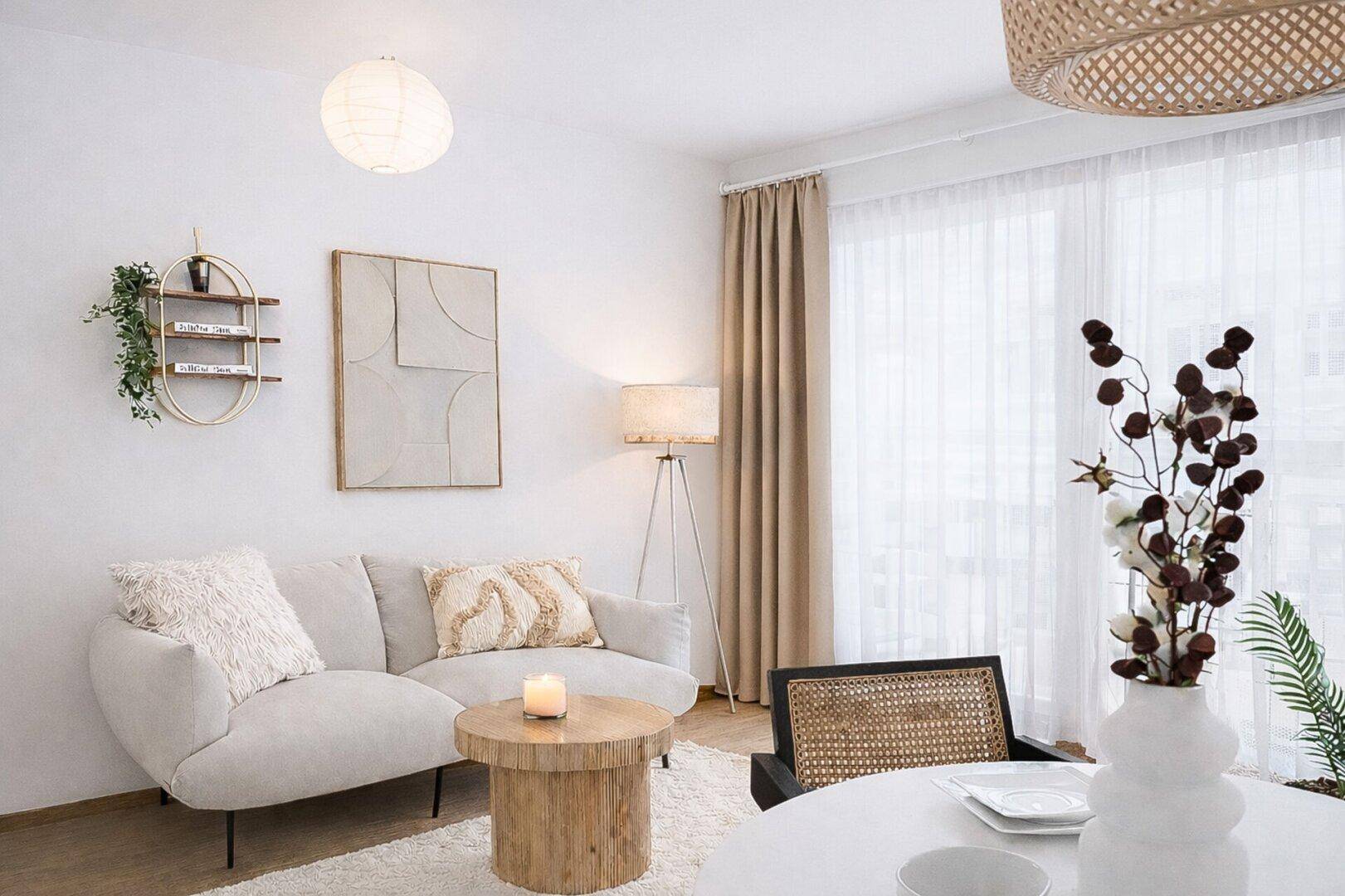 Heller Wohnbereich mit beigem Sofa, Holztisch und großen Fenstern, die eine freundliche Atmosphäre schaffen.