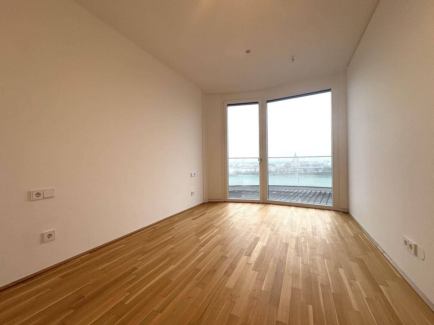 Helles Schlafzimmer mit Parkettboden und Zugang zu einem Balkon mit Blick auf das Wasser.