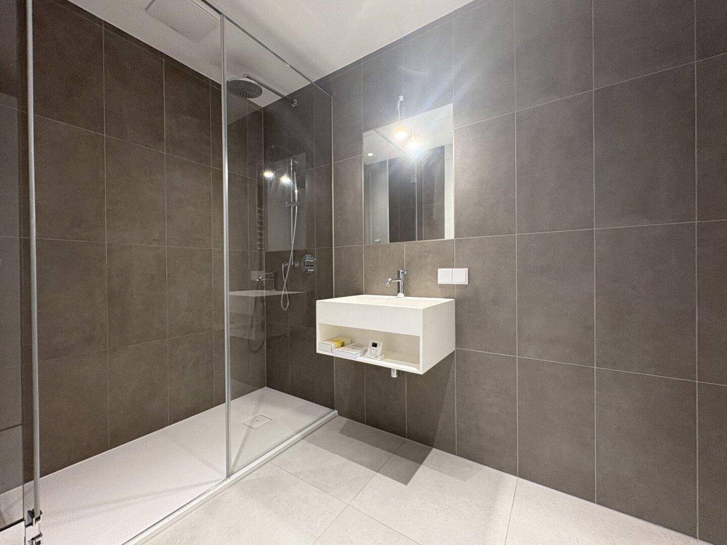Modernes Badezimmer mit großen grauen Fliesen, ebenerdiger Dusche und schwebendem Waschtisch.