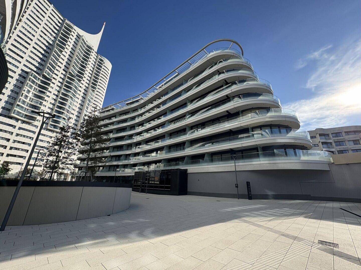 Beeindruckende moderne Architektur mit geschwungenen Balkonen und Glasfassade unter blauem Himmel.