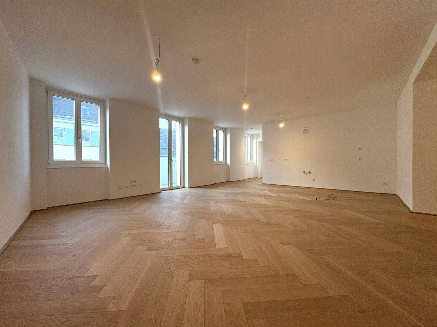 Geräumiger, heller Raum mit Fischgrätparkett und vielen Fenstern, bereit zum Einzug.