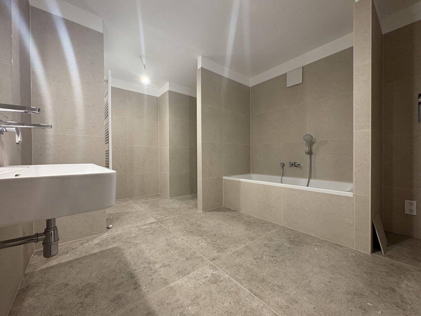 Modernes Badezimmer mit beigefarbenen Fliesen, Einzelwaschbecken und eingebauter Badewanne.
