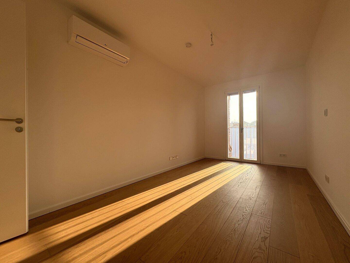 Helles Zimmer mit Holzparkett, Klimaanlage und Zugang zu einem Außenbereich.