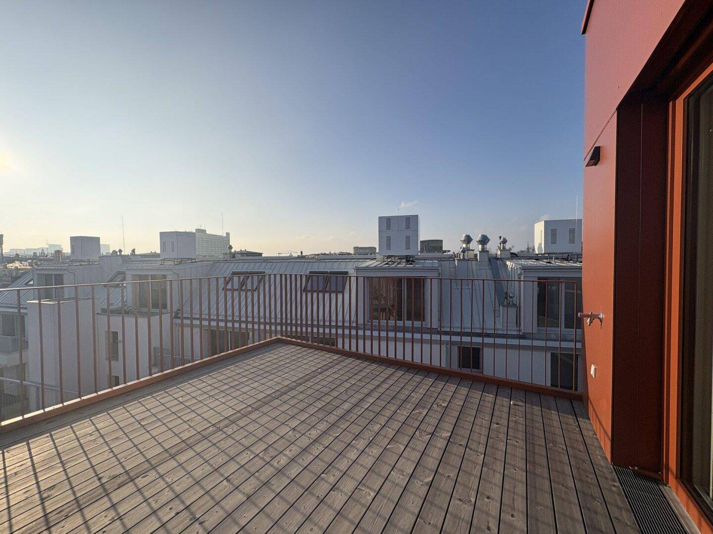 Geräumige Dachterrasse mit Holzdielen und Panoramablick über die umliegenden Dächer.