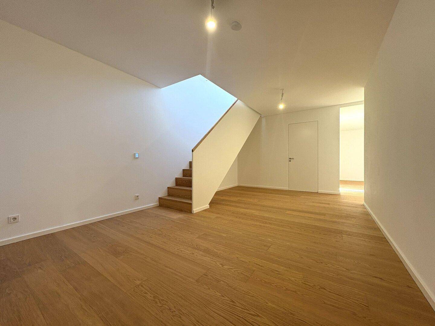 Heller, leerer Raum mit Holzboden und offener Treppe zum Obergeschoss.