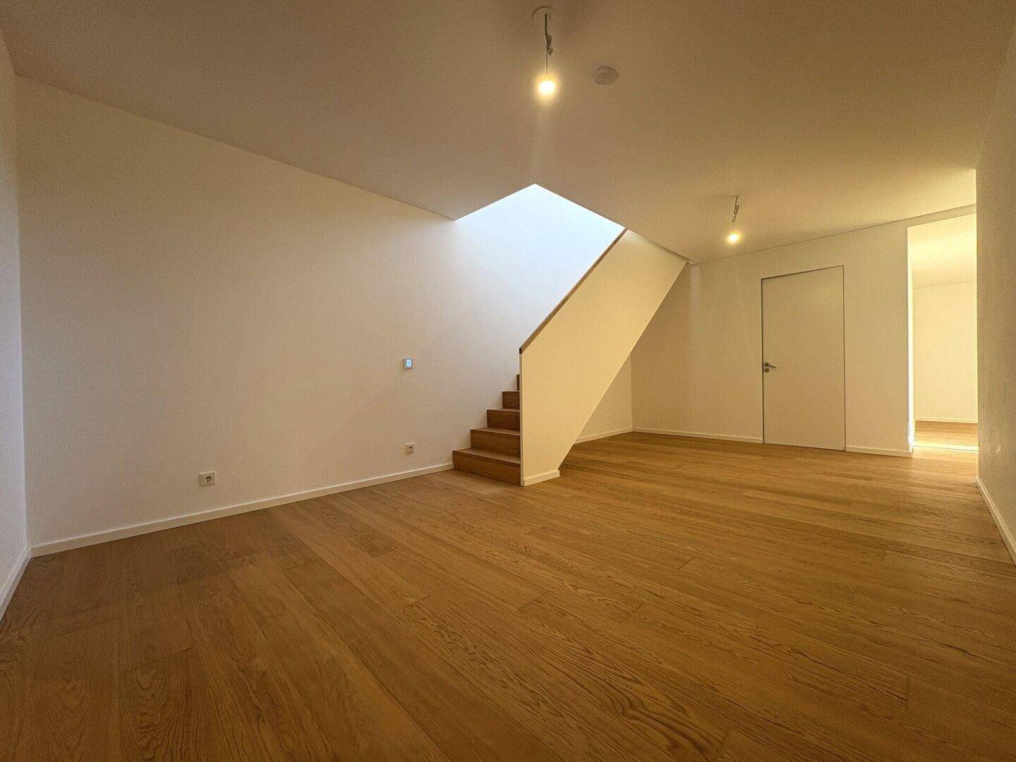 Heller, leerer Raum mit Holzboden und offener Treppe zum Obergeschoss.