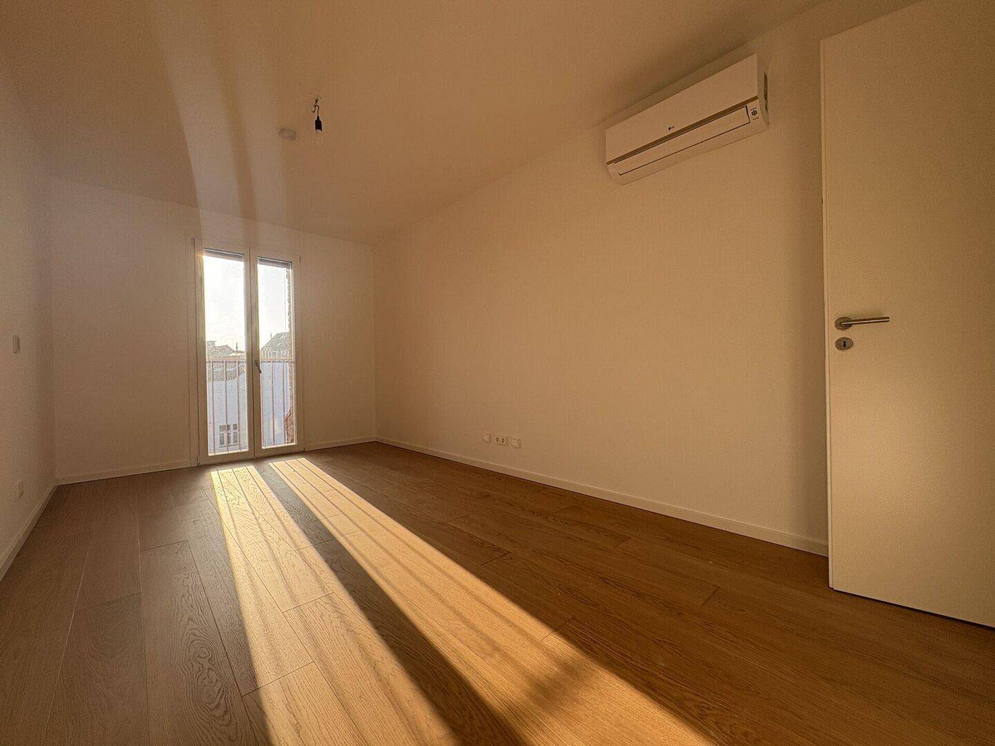 Helles Schlafzimmer mit Holzboden, Klimaanlage und Zugang zu einem französischen Balkon.