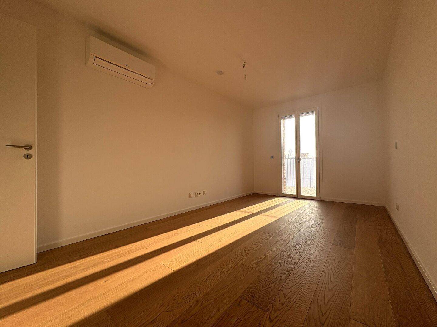 Helles Schlafzimmer mit Holzboden, Klimaanlage und Zugang zu einem französischen Balkon.