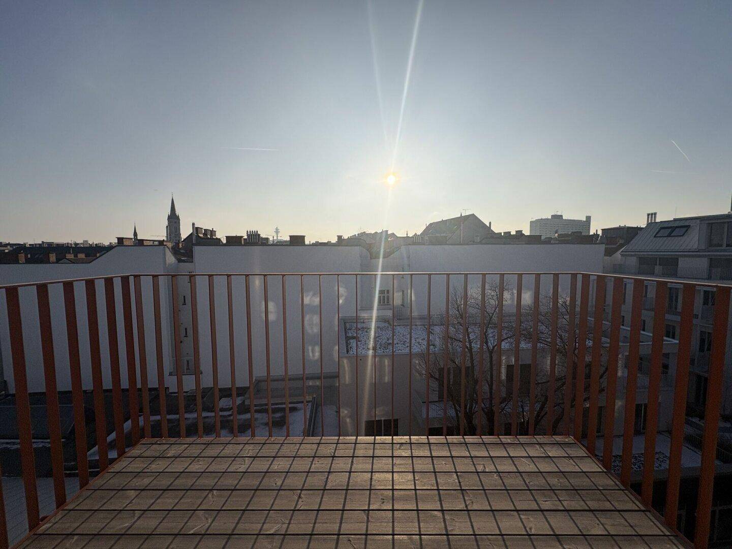 Dachterrasse mit Holzboden und weitem Blick über die Stadt bei Sonnenuntergang.