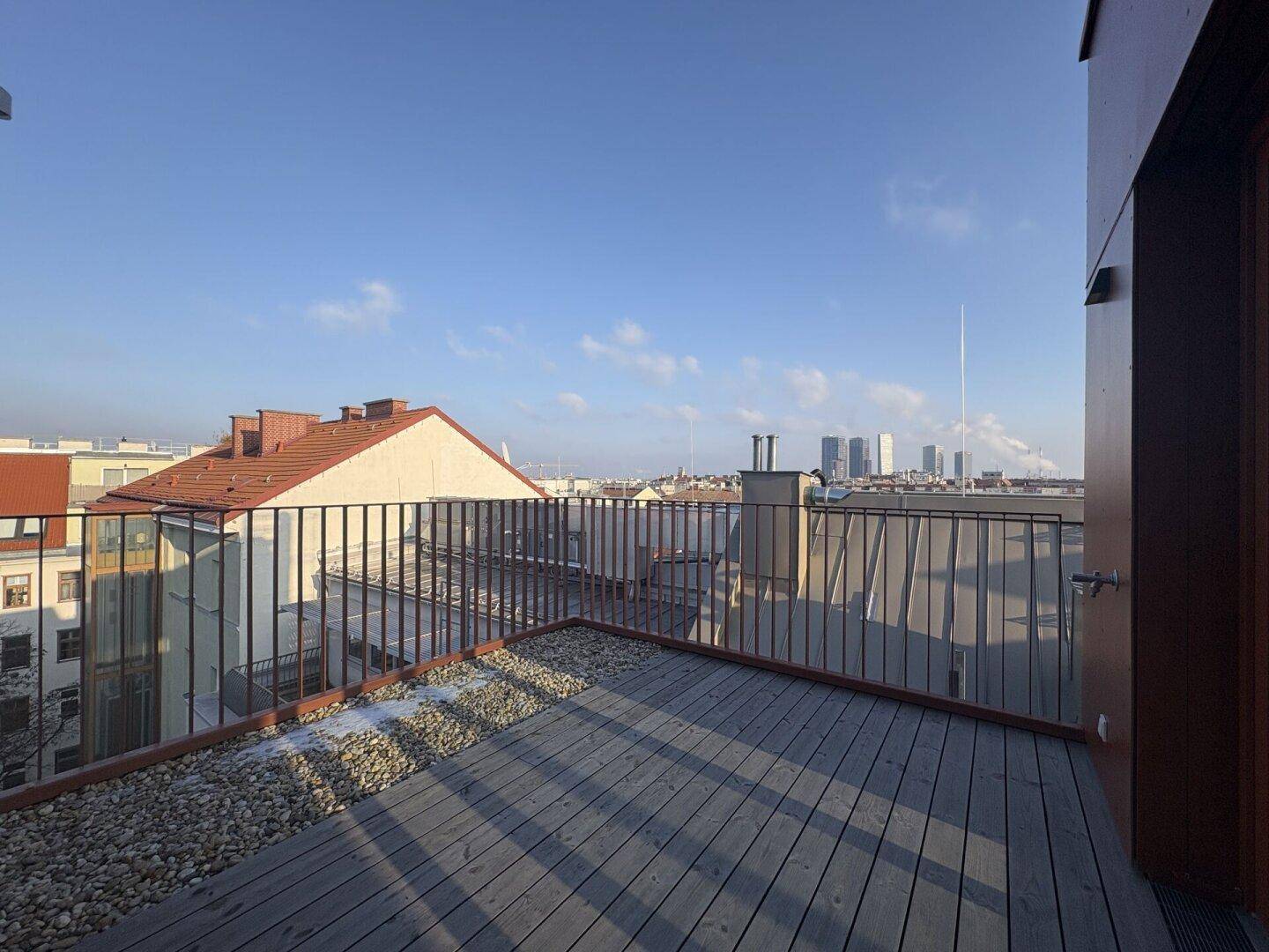 Große Dachterrasse mit Holzboden, Kiesbereich und weitem Blick über die Stadt.
