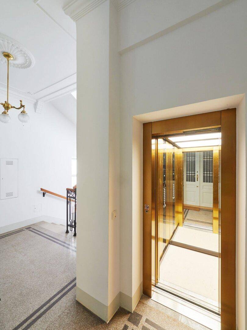 Offener Aufzug mit goldfarbenen Türen in einem eleganten Eingangsbereich mit Terrazzoboden.