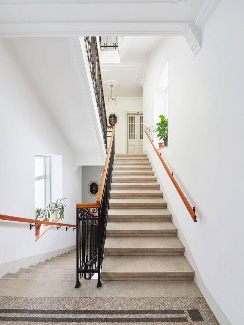 Elegantes Treppenhaus mit Steinstufen, schmiedeeisernem Geländer und Holzhandlauf in einem Altbau.