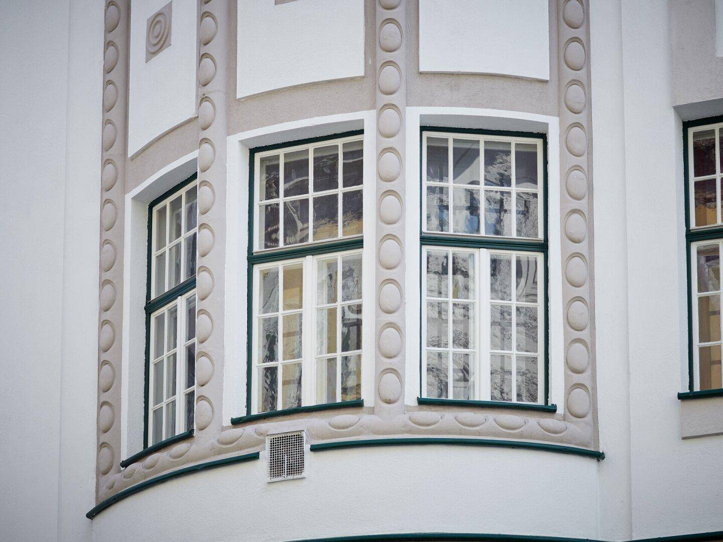 Detail der Altbaufassade mit Erkerfenstern und dekorativen Elementen in Weiß und Grün.