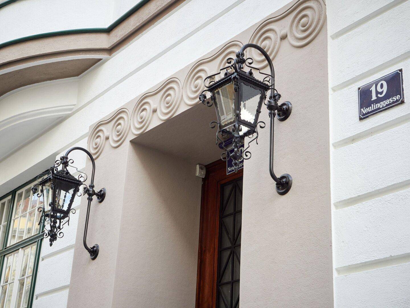 Verzierter Eingangsbereich mit schmiedeeisernen Laternen und dekorativen Stuckelementen an der Fassade.