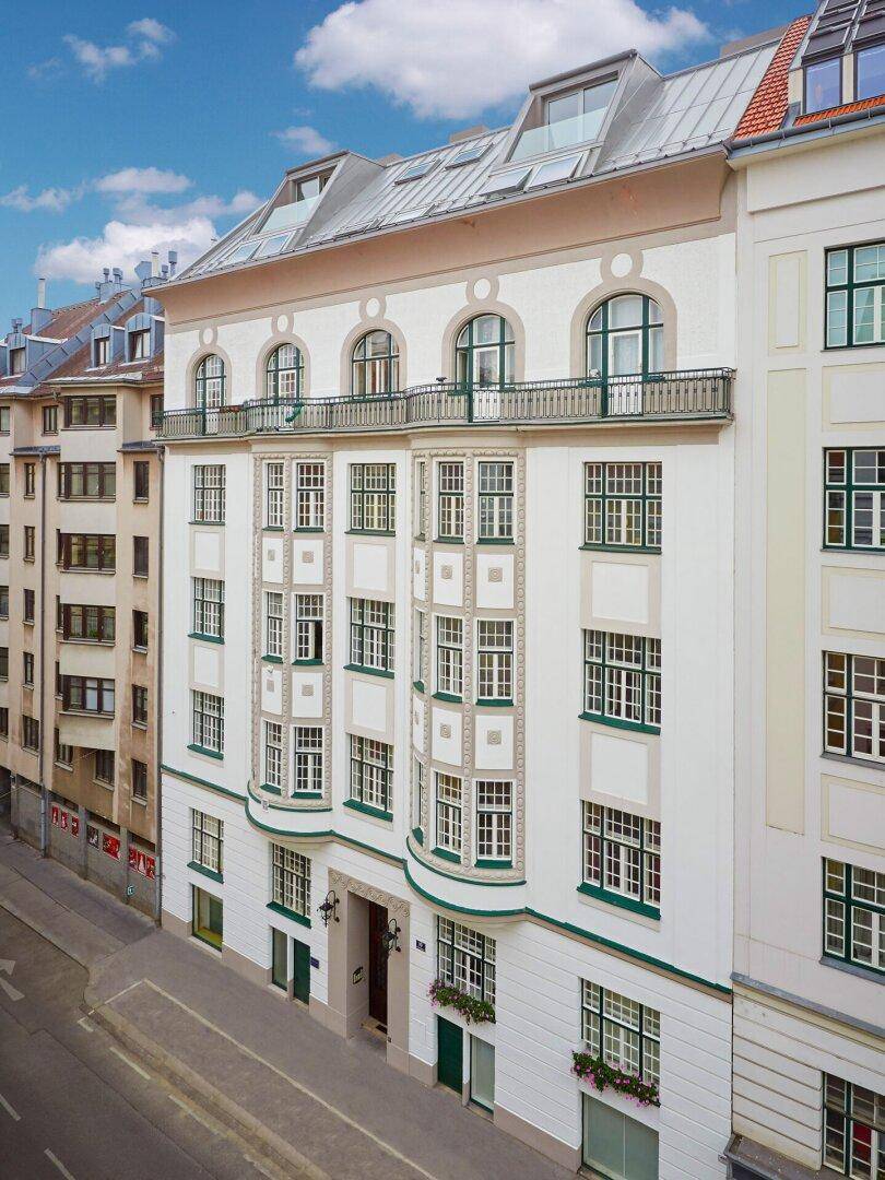 Historisches Gebäude mit eleganter Fassade, Erkerfenstern und einem Balkon im oberen Stockwerk.