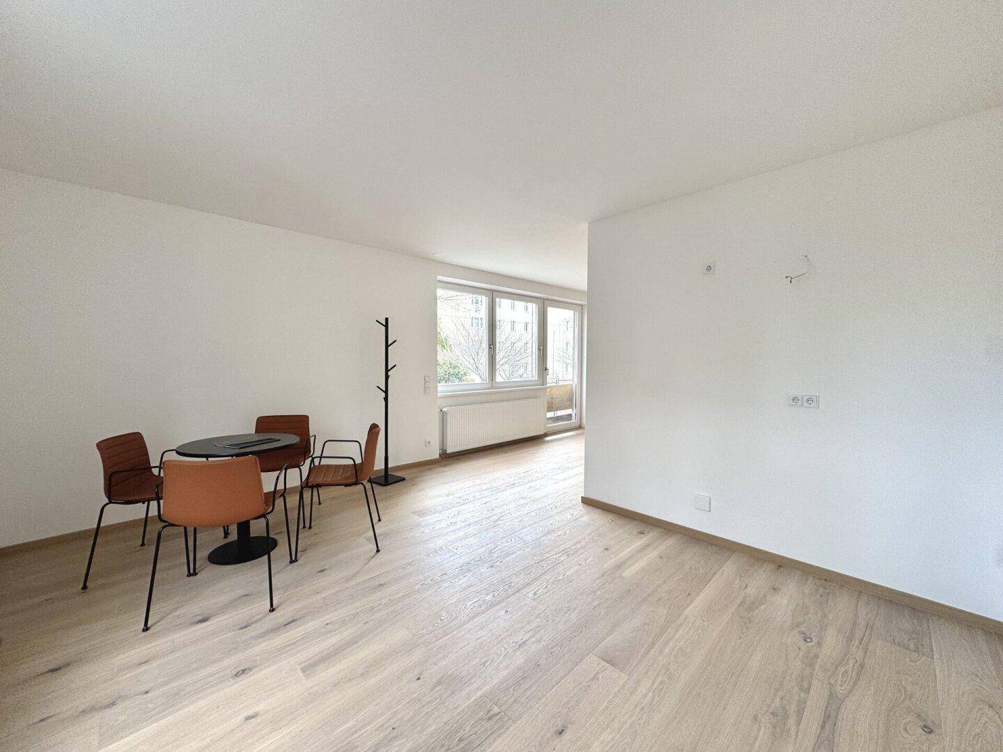 Leerer Raum mit Parkettboden, einem kleinen Esstisch und Garderobe, mit Blick nach draußen.